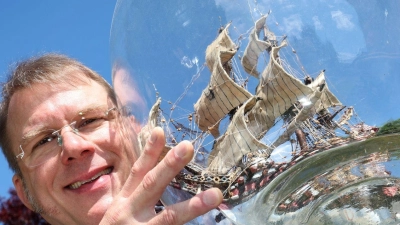 Matthias Schultz hält ein von ihm gebautes 40 Zentimeter hohes und 38 Zentimeter langes Buddelschiff welches in einem 50 Liter fassenden Gärballon hängt. (Foto: Karl-Josef Hildenbrand/dpa)